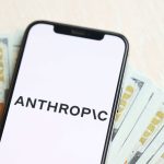Celular com logo da Anthropic posicionado acima de notas de dólar.