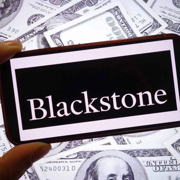 Logo da Blackstone em um smartphone; atrás, várias notas de dólar