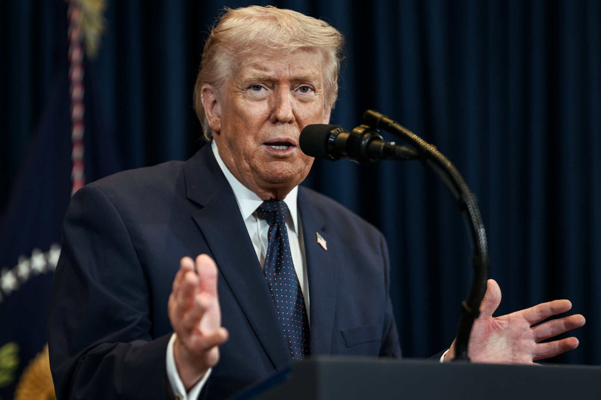 Donald Trump em um púlpito com as mãos abertas e falando em um microfone