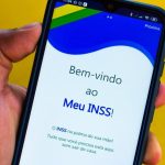 Pessoa segurando celular com aplicativo Meu INSS aberto na tela inicial