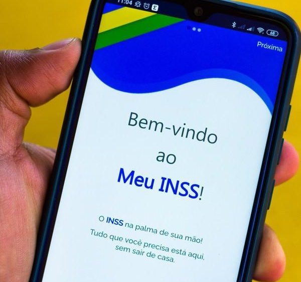 Pessoa segurando celular com aplicativo Meu INSS aberto na tela inicial
