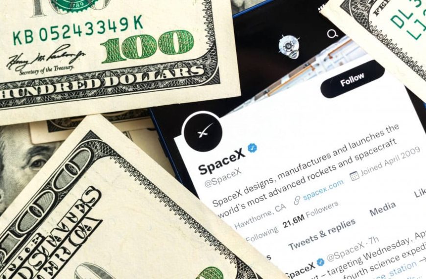 Página da SpaceX no Twitter aberta em celular rodeado de notas de dólar numa mesa