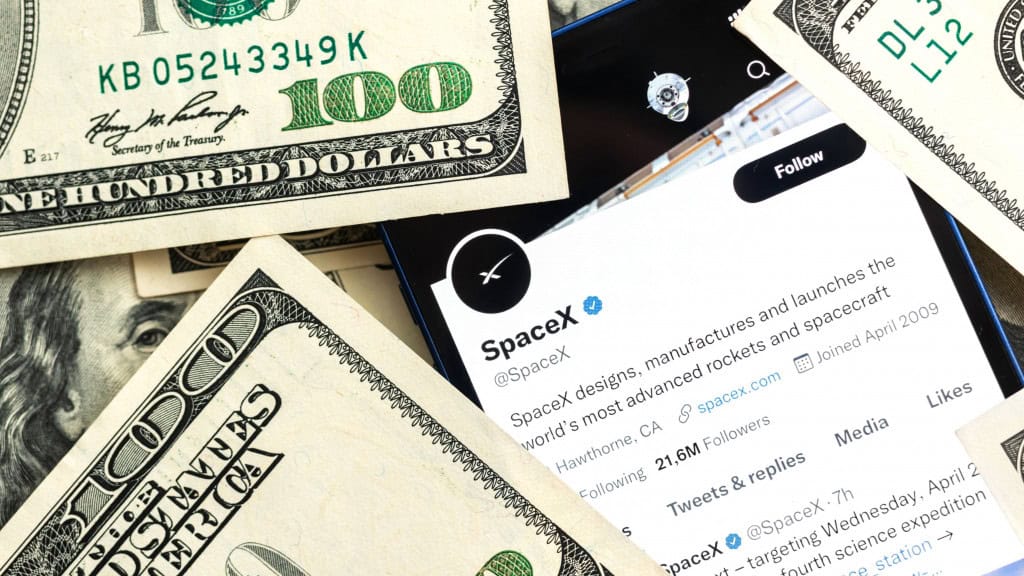 Página da SpaceX no Twitter aberta em celular rodeado de notas de dólar numa mesa