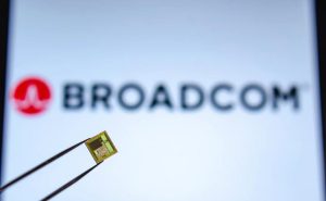 pinça segura um chip em primeiro plano com o logo da Broadcom ao fundo