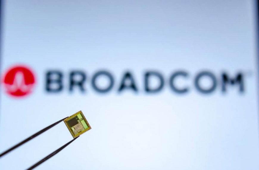 pinça segura um chip em primeiro plano com o logo da Broadcom ao fundo