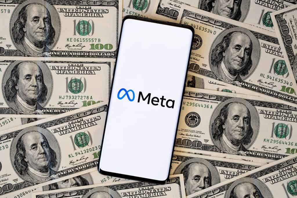 Logo da Meta em um smartphone, que está em cima de várias notas de dólares dos Estados Unidos