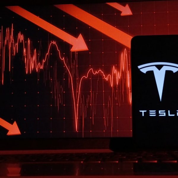 Logo da Tesla em um smartphone com indicadores financeiros atrás